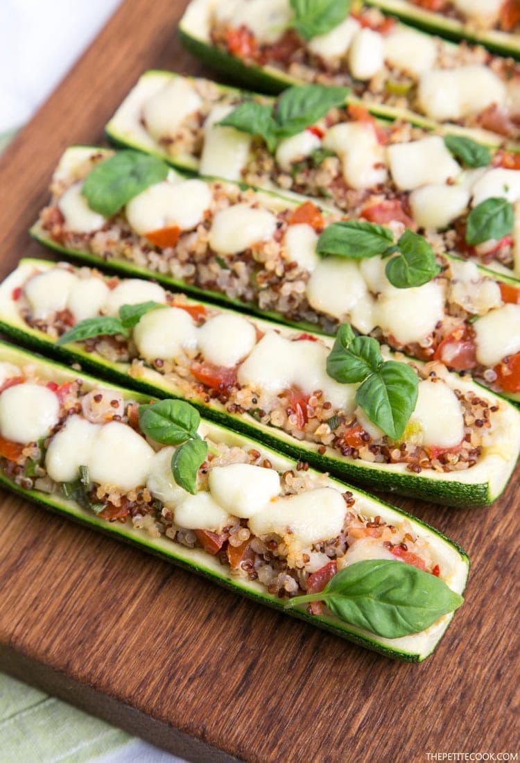 Zucchini boats stuffed qith quinoa and pico de gallo, topped with melted mozzarella cheese and basil leaves, on wood board with green napkin beneath