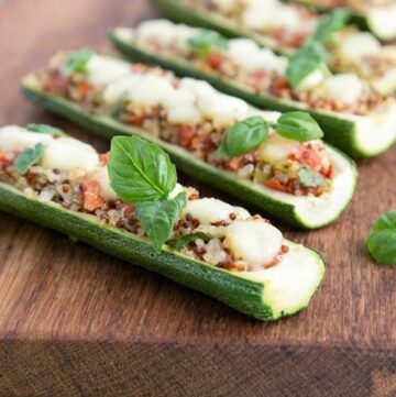 zucchini boats stuffed with quinoa and pico de gallo, topped with melted mozzarella cheese and basil leaves on a wood board