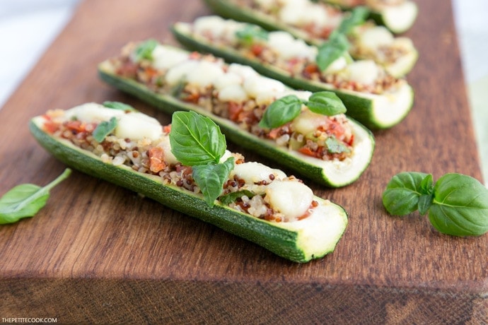zucchini boats stuffed with quinoa and pico de gallo, topped with melted mozzarella cheese and basil leaves on a wood board