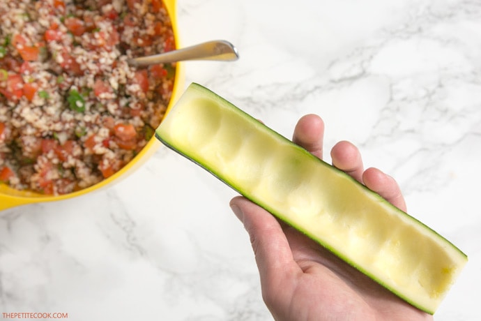 hand holding half zucchini for zucchini boats, quinoa and pico de gallo filling on the left side