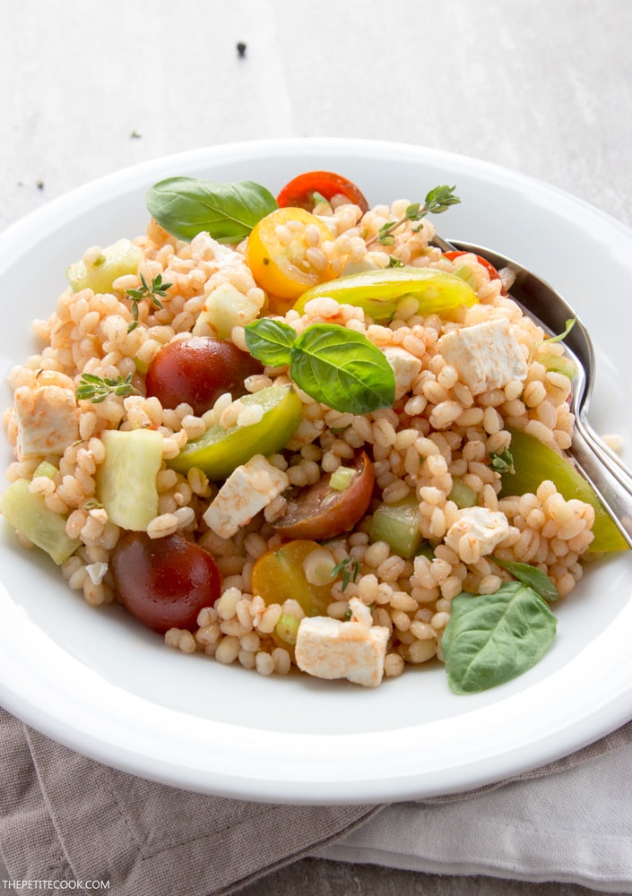 barley greek salad with feta, basil and tomatoes, on a plate.