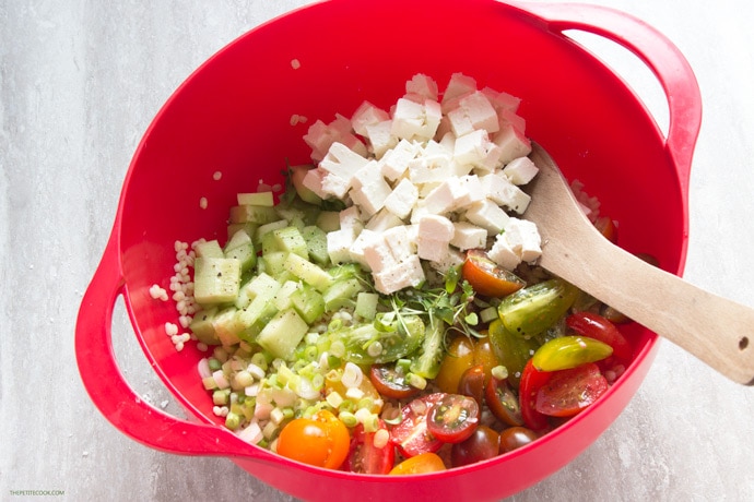 Finely chopped tomatoes, cucumber, spring onion, feta cheese, herbs and cooked pearl barley in a bowl.