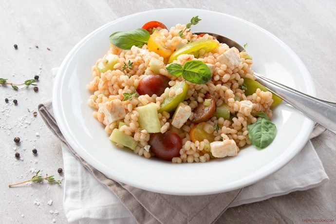 greek barley salad on a plate topped with basil leaves.