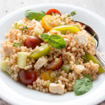 greek barley salad in a plate topped with basil leaves