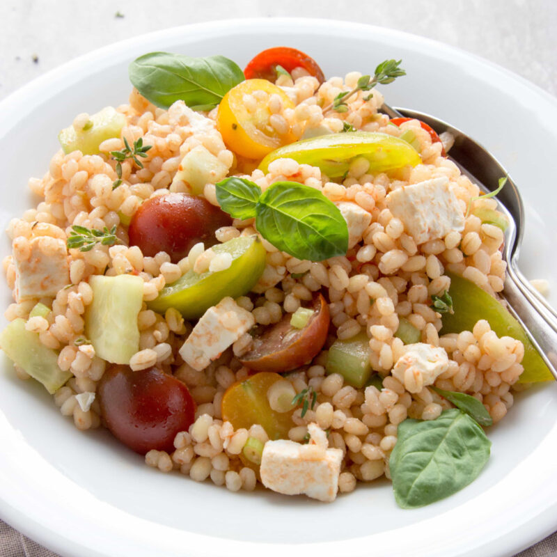 greek barley salad in a plate topped with basil leaves