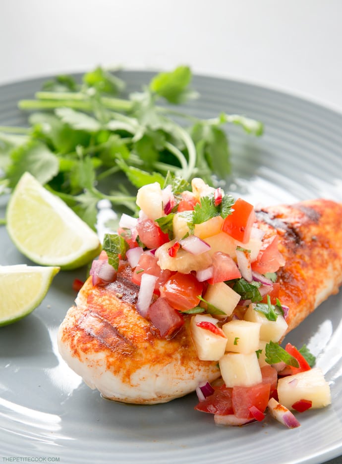 tequila lime chicken topped with pineapple salsa, served lime wedges and cilantro on the side on a grey plate