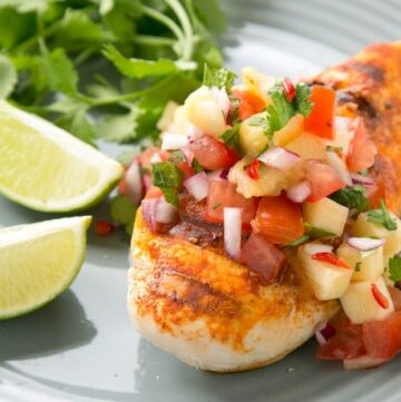 tequila lime chicken topped with pineapple salsa, served lime wedges and cilantro on the side on a grey plate