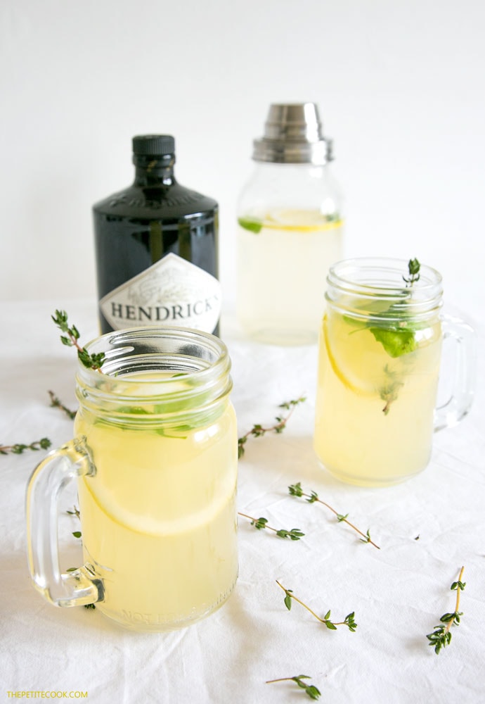 gin lemon with thyme and basil divided among two glasses, bottle of Hendricks gin in the background