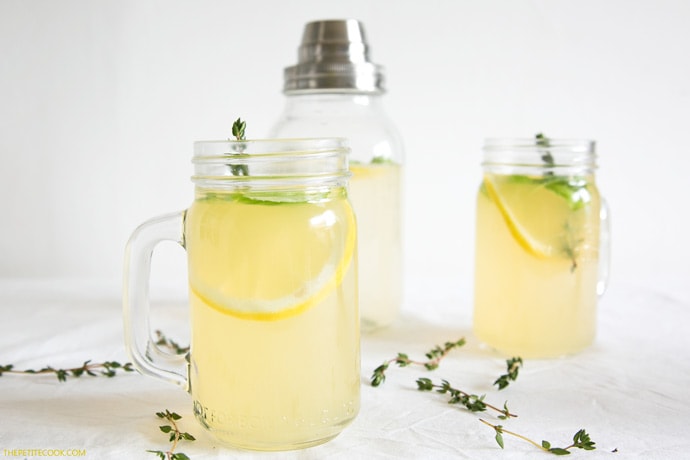 gin lemon with herbs divided among two drinking glasses and a mixing jug