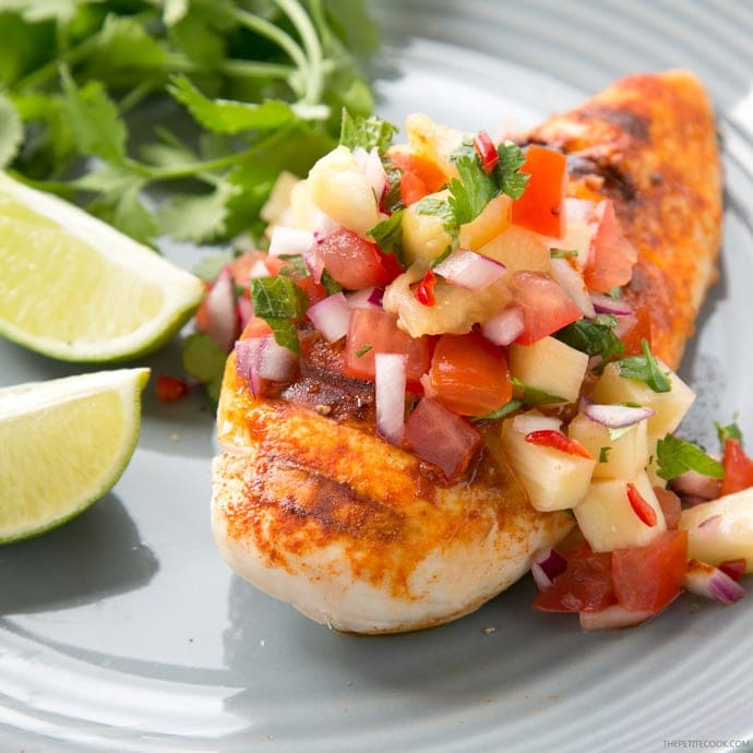 tequila lime chicken topped with pineapple salsa, served lime wedges and cilantro on the side on a grey plate