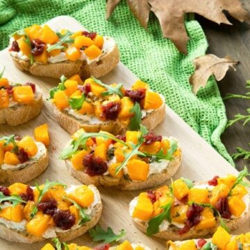 roasted pumpkin bruschetta over wood board with a green cloth on the right