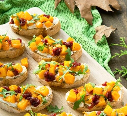 roasted pumpkin bruschetta over wood board with a green cloth on the right
