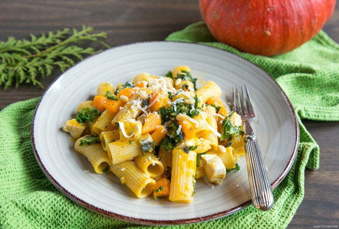 pasta with pumpkin kale and chicken on a plate with a fork and a pumpkin on the background