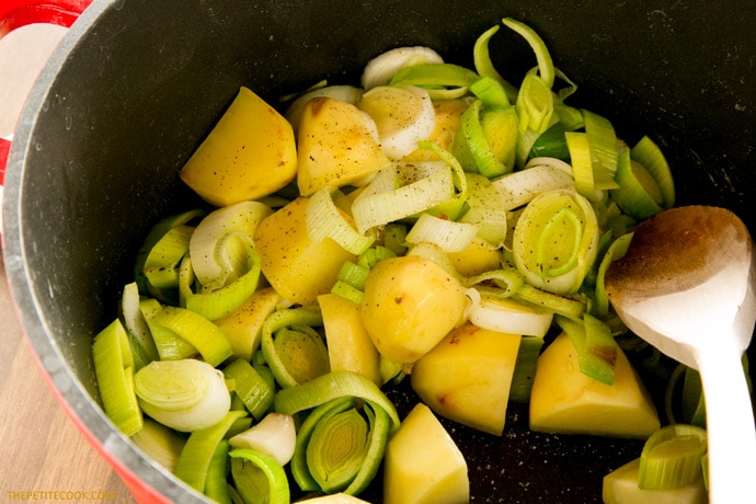 Cubed Potatoes, sliced leeks and a wood spoon in a large cast iron pot.