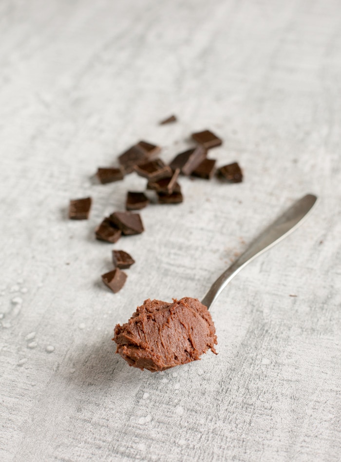 chocolate frosting on a spoon, chopped chocolate bar in the background