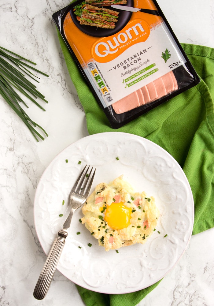 eggs in a cloud on a white plate with fork on the side over a green napkin, quorn vegetarian bacon package on the top side and chives on the left side