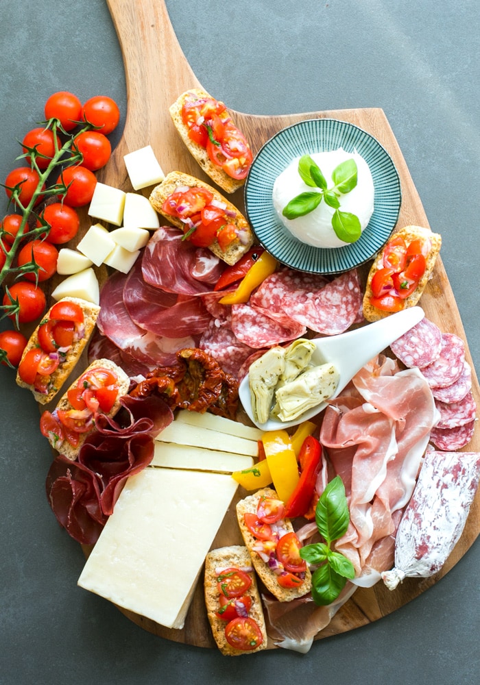 Aperitivo platter featuring mozzarella ball, cured meats, bruschetta, artichokes in olive oil, and  cubed cheese.