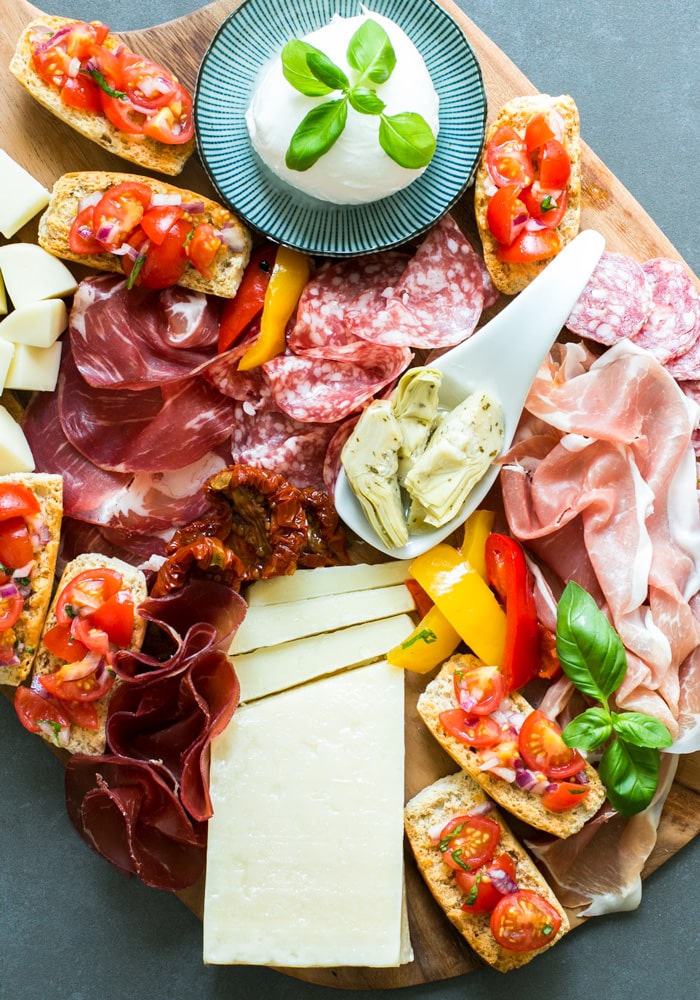 Aperitivo platter featuring mozzarella ball, cured meats, bruschetta, artichokes in olive oil, and  cubed cheese.