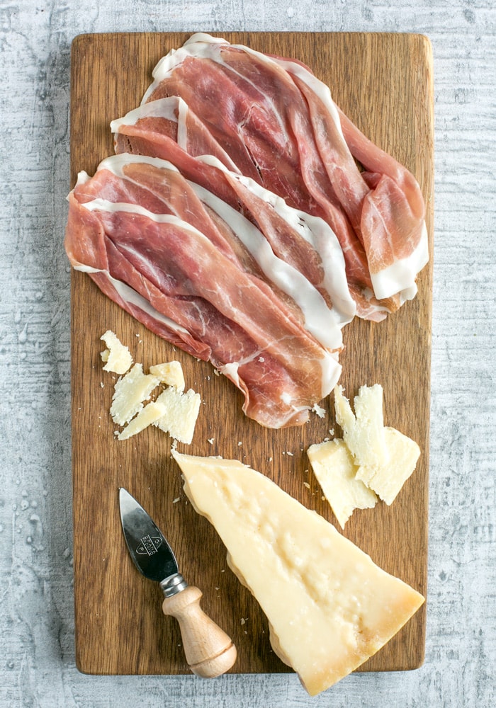 prosciutto san daniele slices and grana padano cheese piece, and cheese knife on a wood board