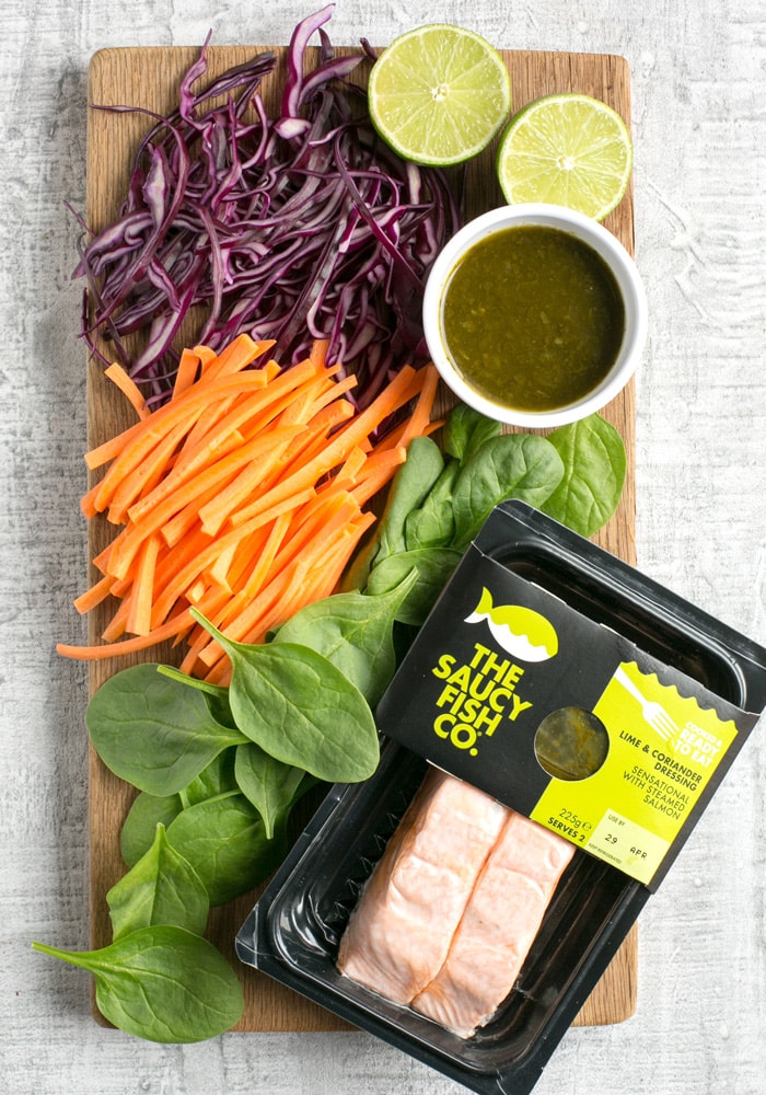 Vietnamese summer rolls ingredients: sliced purple cabbage, carrots, spinach leaves, halved lime, salmon fillets.