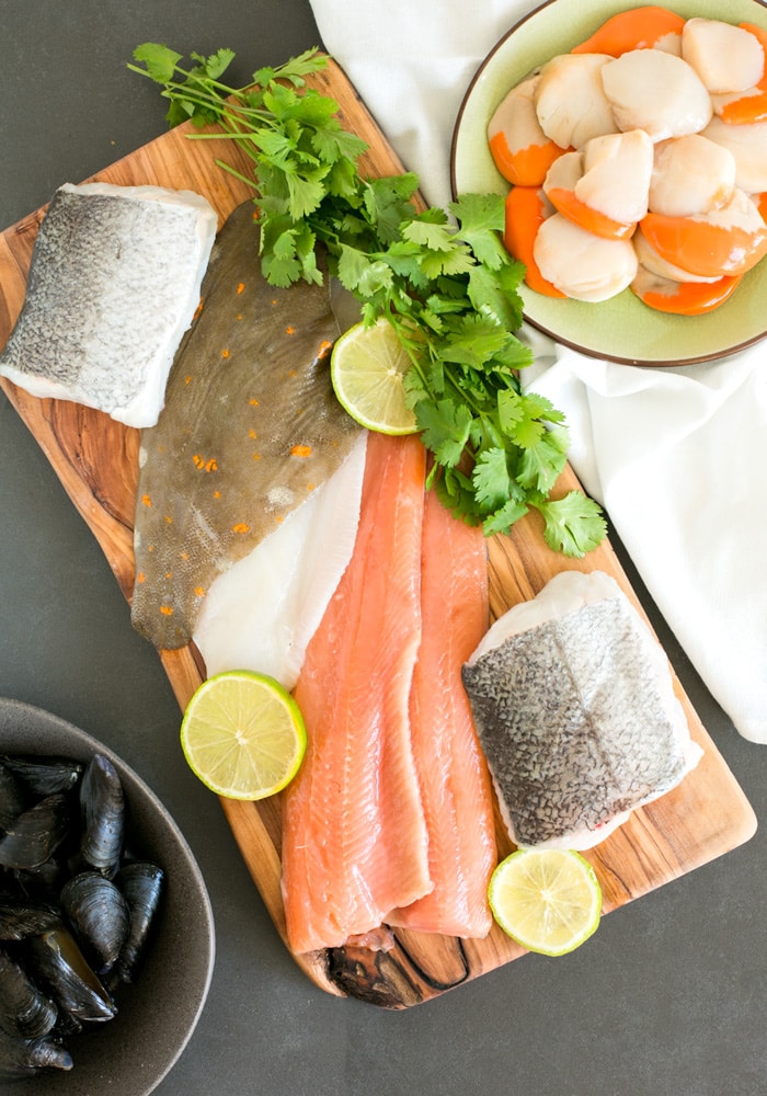 mussels and fish fillets on wood board with parsley and lemon, plate with scallops on white cloth on the side