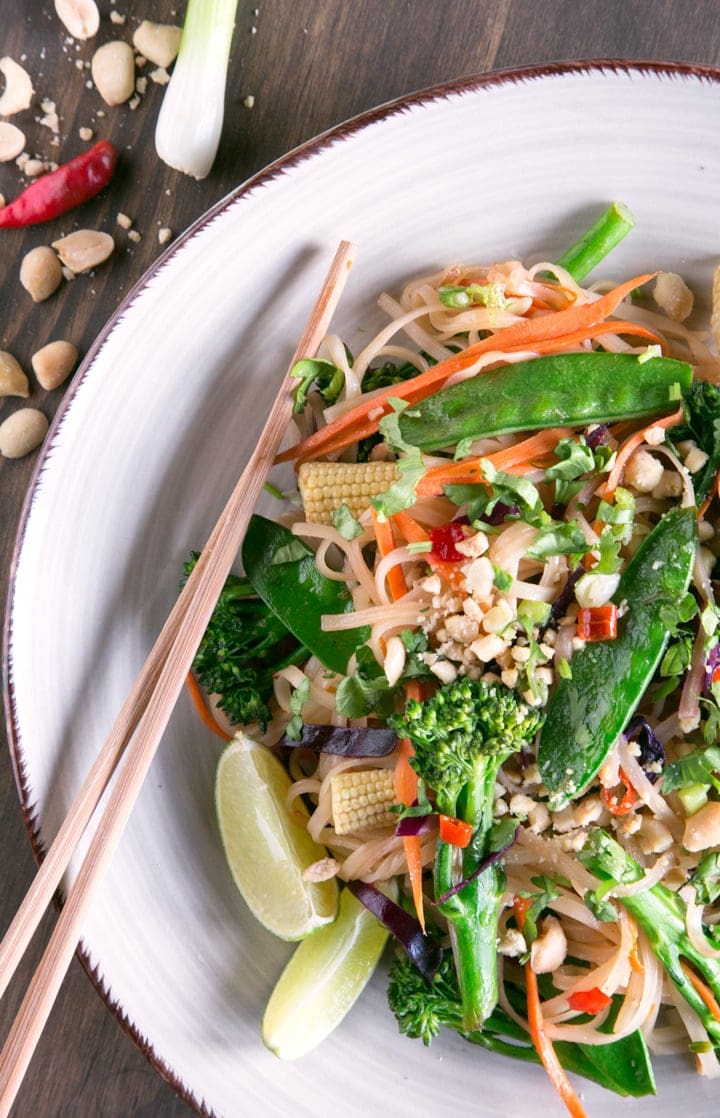 Vegan pad thai topped with roasted peanuts, served with lime wedges.