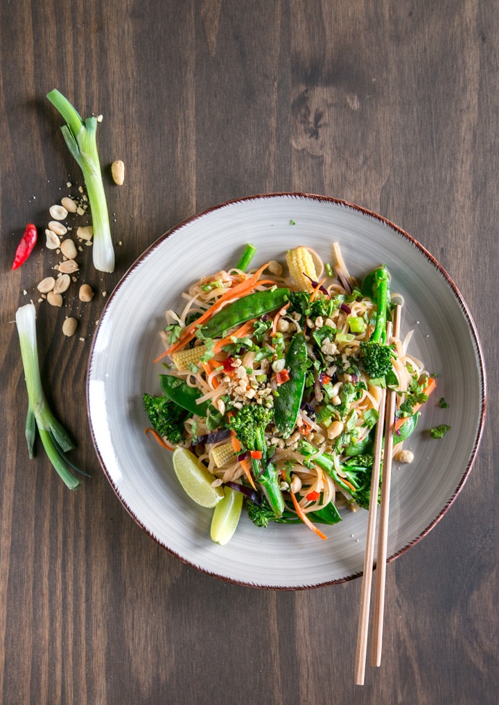 Pad thai with vegetables topped with roasted peanuts and served with lime wedges.