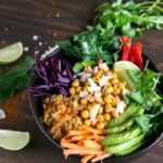 chickpea and freekeh buddah bowl with sliced avocado and carrots and salad leaves.