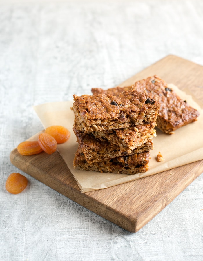 Vegan fruit flapjacks on a wood board covered with parchement paper, dried apricots on the left