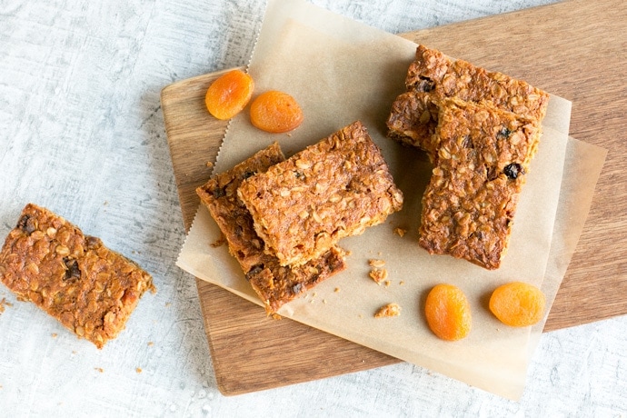 Vegan fruit flapjacks on a wood board covered with parchement paper, dried apricots on the left