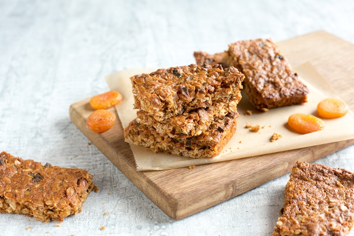 Vegan fruit flapjacks on a wood board covered with parchment paper, dried apricots on the left