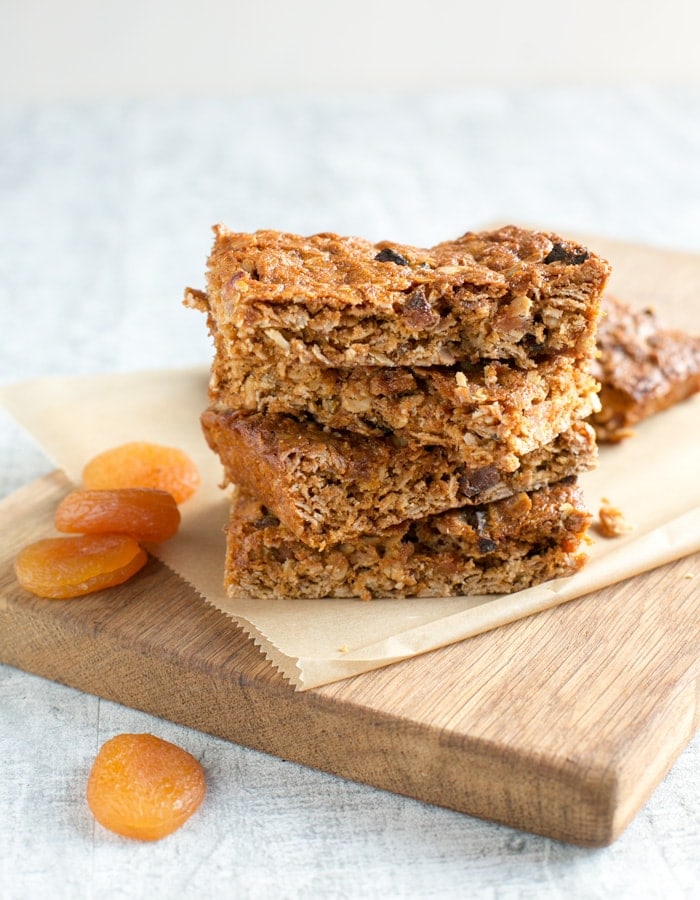 Vegan fruit flapjacks on a wood board covered with parchement paper, dried apricots on the left