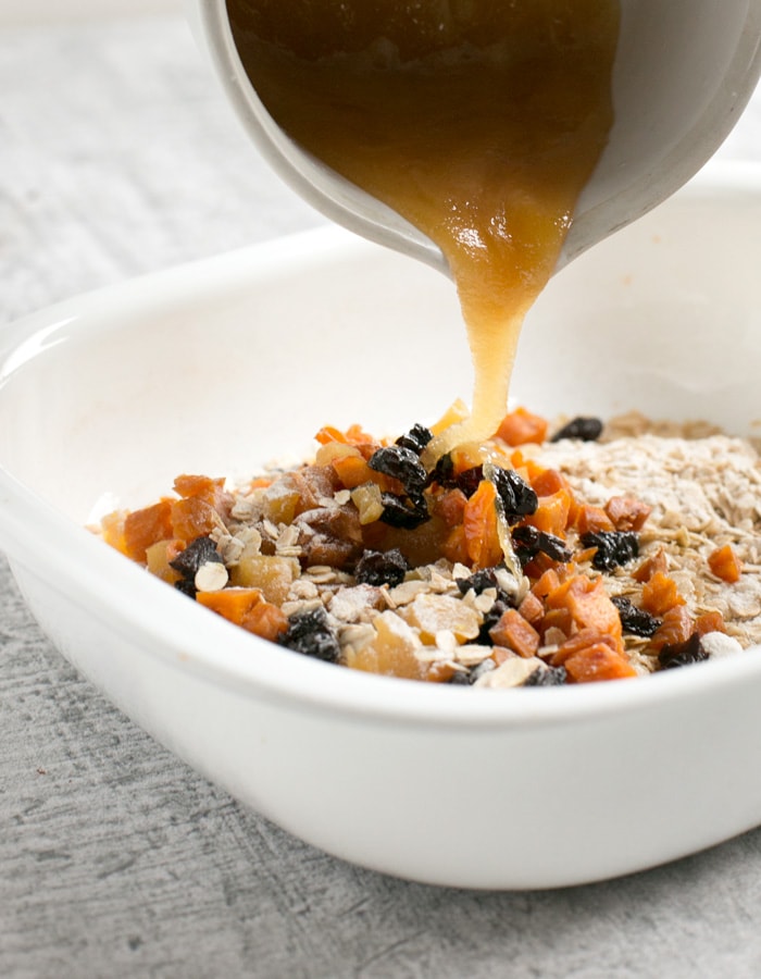 Vegan fruit flapjacks method: dried ingredients in a white casserole dish, wet ingredients in a small white cup slowly poured into the dry mixture 