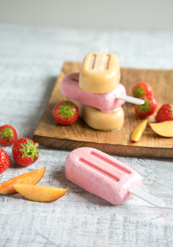 Nectarine and Strawberry Smoothie Popsicles on wood plate, strawberry popsicle on the foreground, strawberries and slices of nectarines scattered around