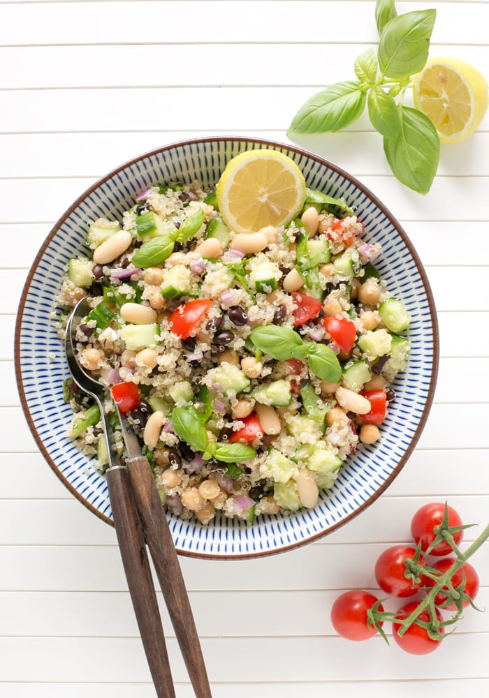 quinoa and bean salad topped with half lemon and lemon leaves in a large bowl with serving spoons.