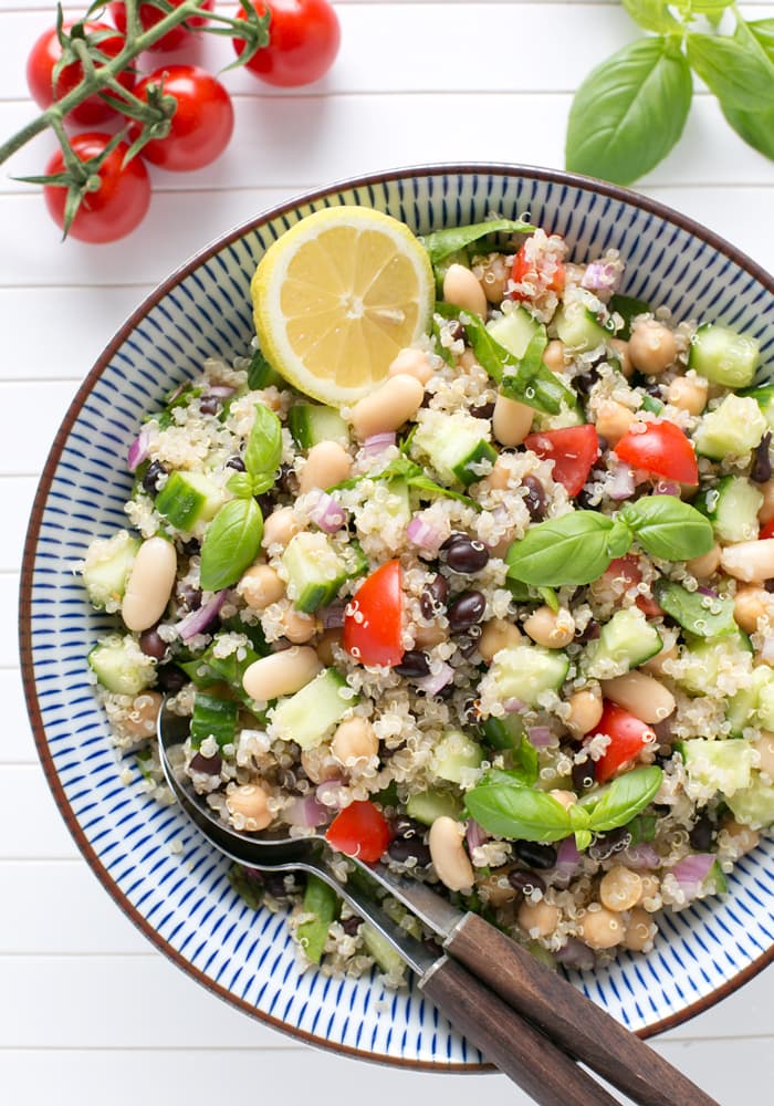 quinoa and bean salad in a large bowl, with half lemon and basil leaves on top.