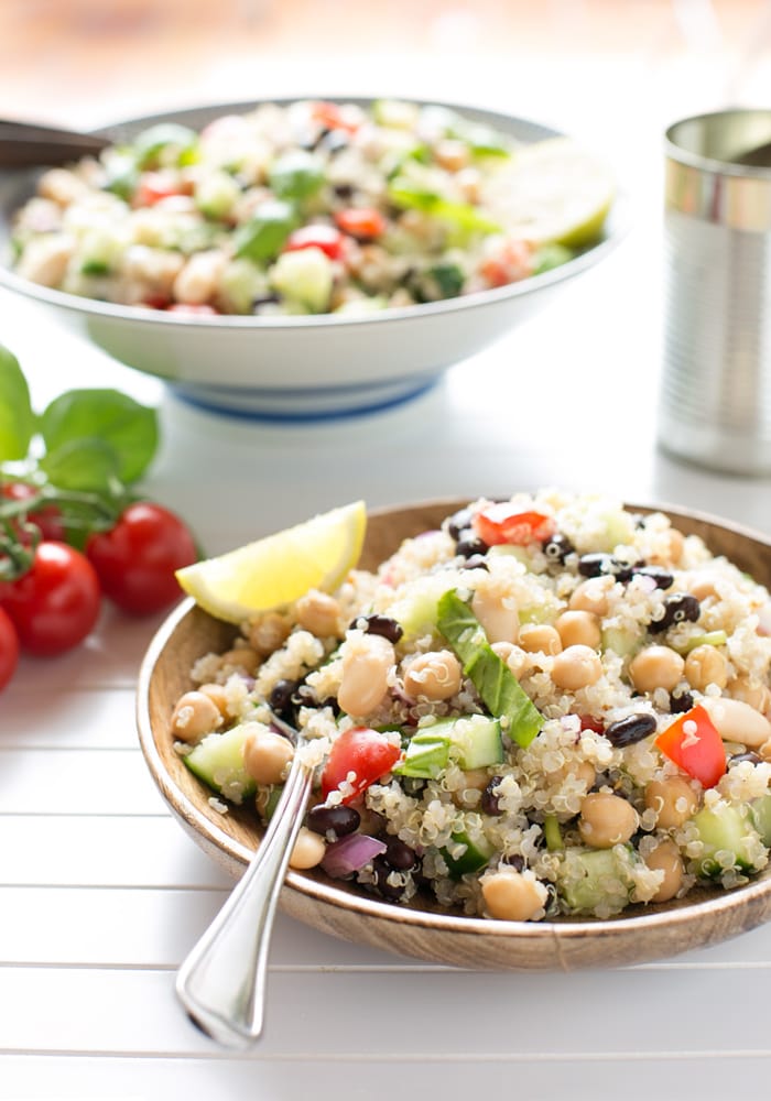 quinoa and bean salad topped with half lemon and lemon leaves in a serving plate with a fork, more salad in a bowl in the background.