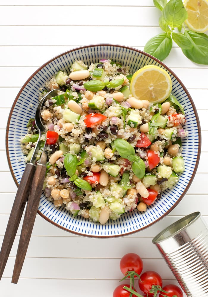 quinoa and bean salad topped with half lemon and basil leaves on a large bowl with serving spoons.