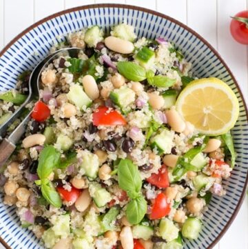 quinoa and bean salad topped with basil leaves and half lemon in a large bowl with serving spoons