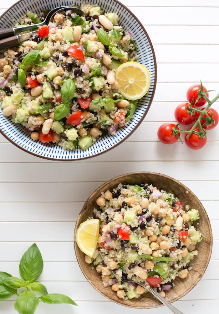 quinoa and bean salad in a large bowl and in a serving plate, both topped with lemon wedges and basil leaves