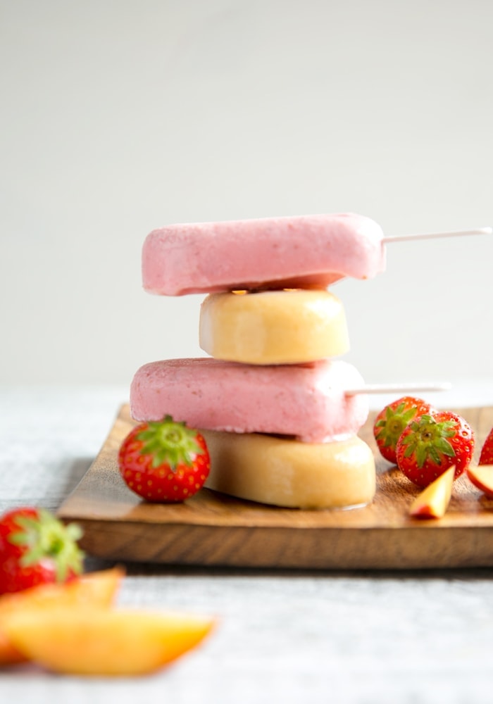 Nectarine and Strawberry Smoothie Popsicles on wood plate, strawberries and slices of nectarines scattered around