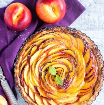 nectarine tart over a purple napkin, two nectarines on the top, half nectarine and a knife on the bottom,
