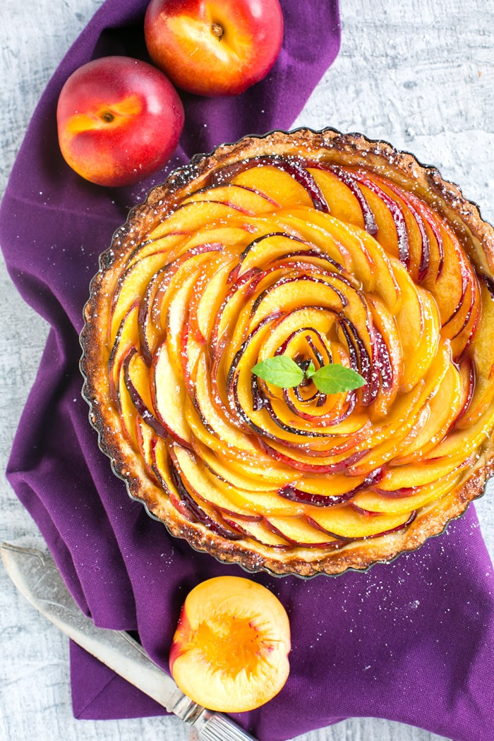 nectarine tart over a purple napkin, two nectarines on the top, half nectarine and a knife on the bottom, 