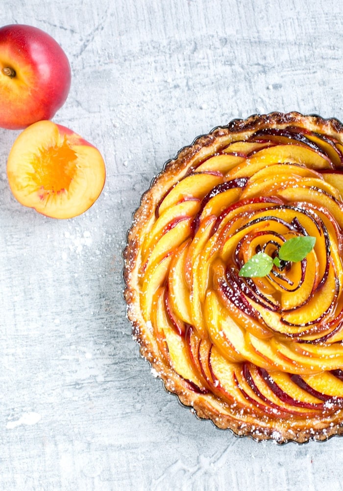 nectarine tart over grey background, one nectarine on the top left side next to half nectarine.