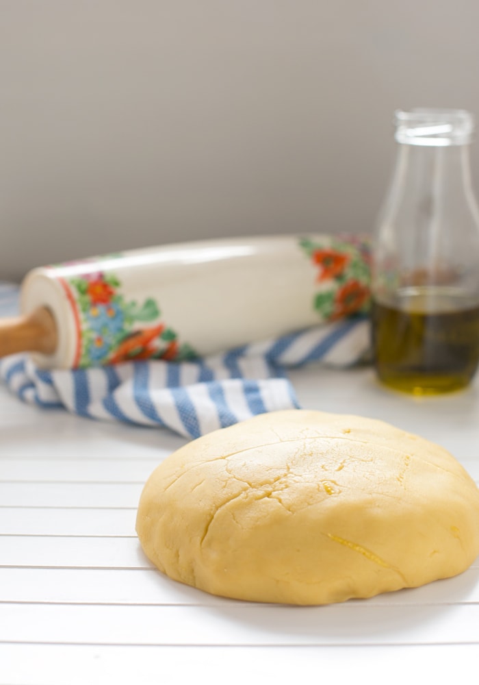 olive oil shortcrust pastry on a white wood board, olive oil in a glass bottle and rolling pin on a striped kitchen cloth in the background