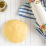 olive oil shortcrust pastry on a white wood board, olive oil in a glass bottle and rolling pin on a striped kitchen cloth