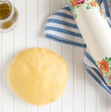 olive oil shortcrust pastry on a white wood board, olive oil in a glass bottle and rolling pin on a striped kitchen cloth