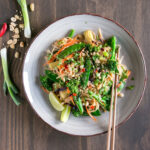 vegan pad thai topped with roasted peanuts and served with lime wedges and chopsticks.