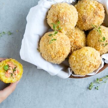 salmon and pea baked arancini rice balls in a dish covered with white napkin, on the left side hand holding half arancini ball