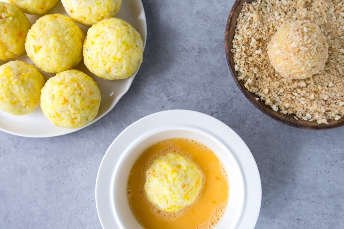 rice balls on a plate, rice ball dipped in whisked eggs on a plate, rice ball rolled into breadcrumbs on a plate